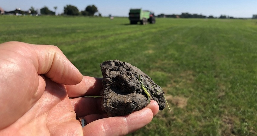 Foto van hand die een kluit grond vasthoudt tegen een achtergrond van een weiland met een wegrijdende tractor